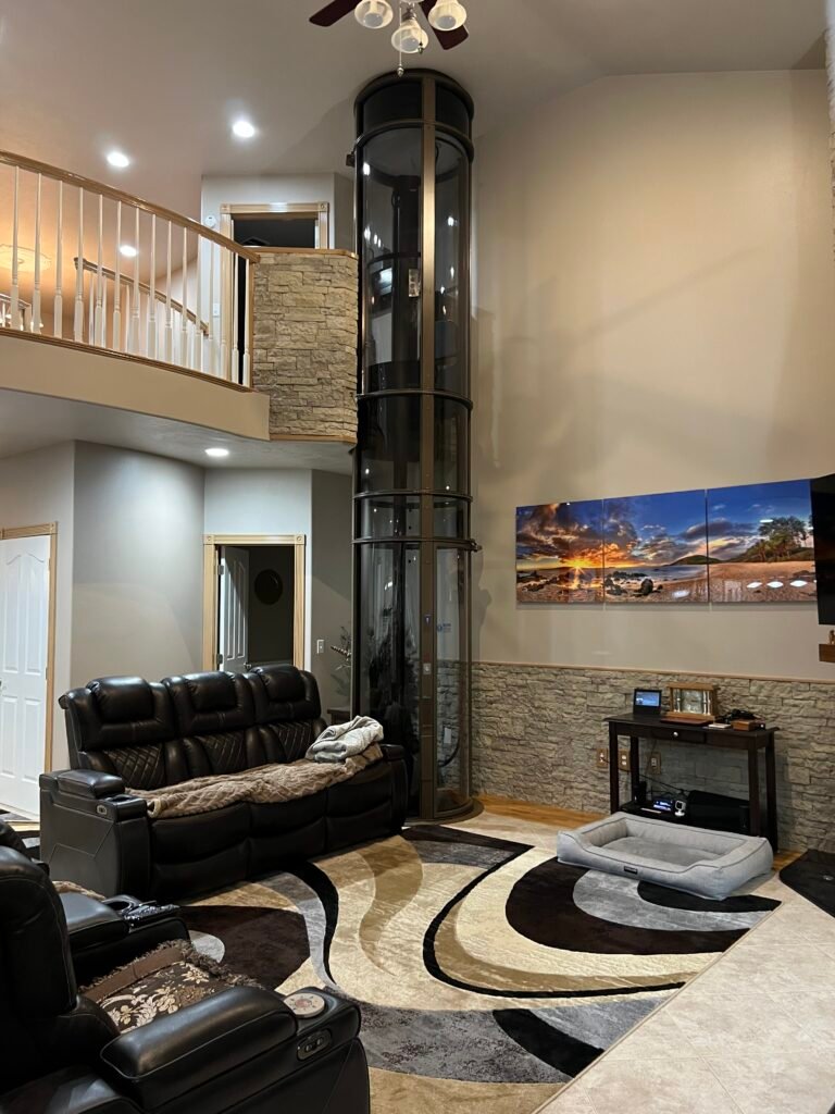 Finished 3-stop pneumatic home elevator installed in luxury DFW living room with stone accent wall and open staircase